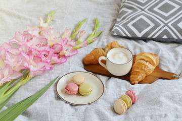 Obraz na płótnie Canvas Croissant, coffee cup, macaroons, flowers in romantic style on bed