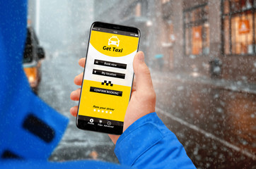 Man on the street booking taxi with smartphone while snowing