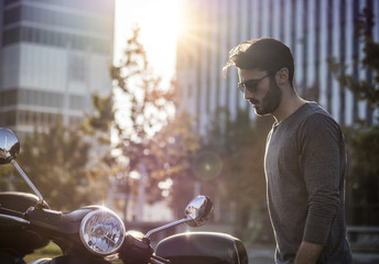 Young handsome man sitting on scooter in backlit on city street.