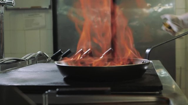 Chef doing flambe to dish in pan with large fire flame in seafood restaurant