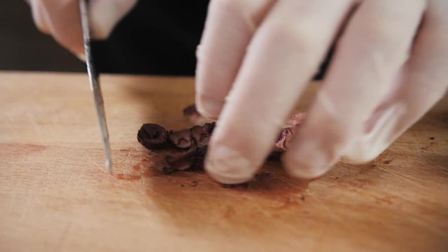 Chef hand holding octopus and tentacles with knife. Seafood restaurant close up slice cut