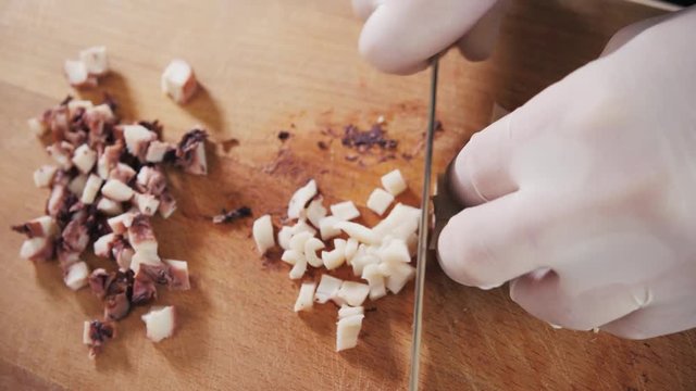 Chef hand holding octopus and tentacles with knife. Seafood restaurant close up slice cut