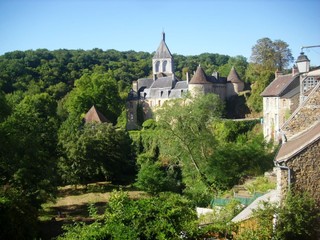 Fototapeta na wymiar Château de Gargilesse entouré d'arbres. Détail du village au premier plan sur la droite. Colline boisée et ciel bleu en arrière-plan. 