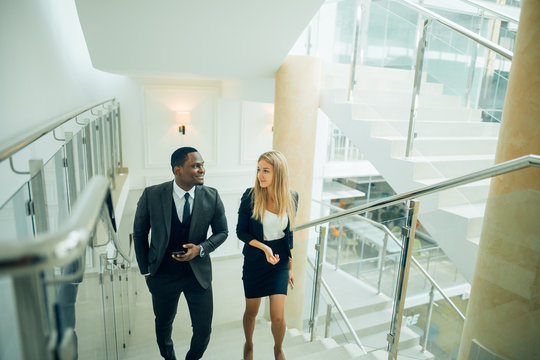 Businessman and Business woman walking up stairs with bags to office.