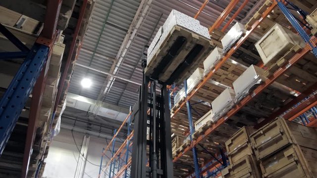 warehouse worker driver in uniform loading cardboard boxes by forklift stacker loader furnirure storage boards