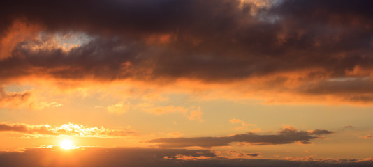 Naklejka na ściany i meble Beautiful sunset on sky. Gold sun lightens the clouds. The sun is on the left side.