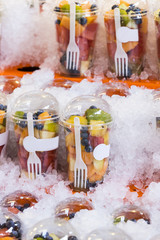 Fresh fruit in plastic cups on a showcase with ice.