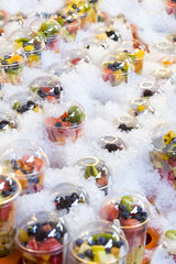 Fresh fruit in plastic cups on a showcase with ice.