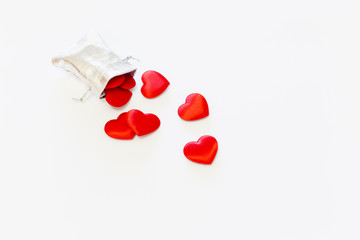 Close-up of a small shiny silver bag filled with cute red velvet hearts on white background. Concept of a romantic love gift for couples, valentines day, marriages or birthdays.