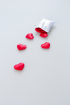Close-up of a small shiny silver bag filled with cute red velvet hearts on light gray background. Concept of a romantic love gift for couples, valentines day, marriages or birthdays.