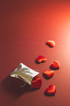 Close-up of a small shiny silver bag filled with cute red velvet hearts on red background. Concept of a romantic love gift for couples, valentines day, marriages or birthdays.
