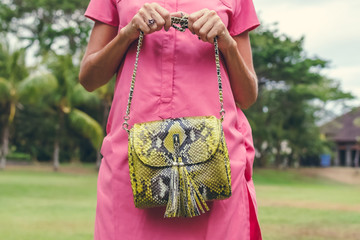 Closeup attractive beautiful woman with snakeskin python handbag posing outdoors. Bali island.