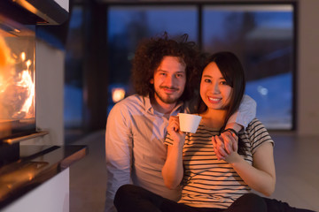 happy multiethnic couple sitting in front of fireplace