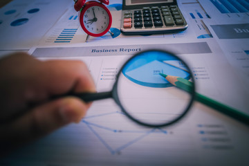 Many charts and graphs with magnifying glass and many pencil. Reflection light and flare. Concept image of data gathering and statistical working.