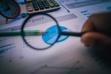 Many charts and graphs with magnifying glass and many pencil. Reflection light and flare. Concept image of data gathering and statistical working.