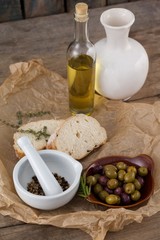 Olives with oil bottle and bread by spices in mortar pestle on