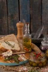 Ingredients with olives in container by bread on cutting board