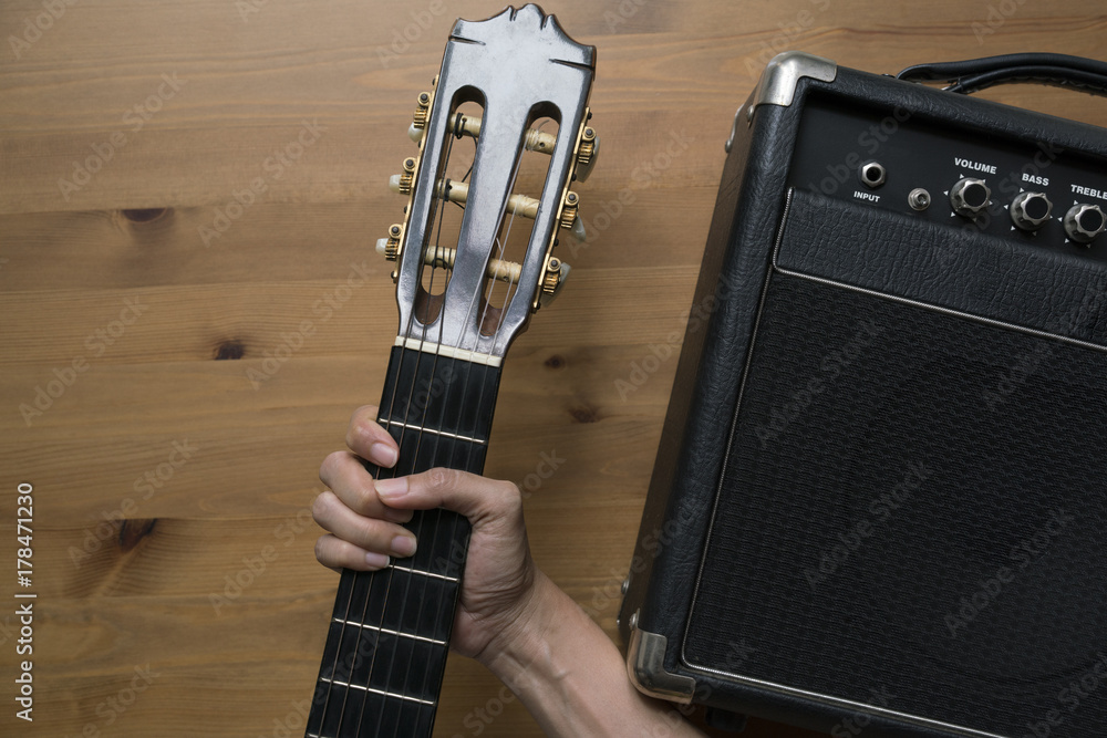 Wall mural Guitar amplifier and woman hand holding a guitar on wood table