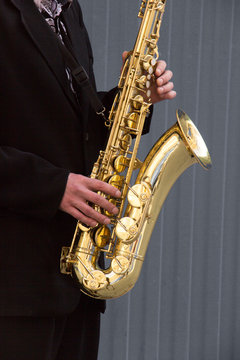 Hands of groom play on saxophone on grey background