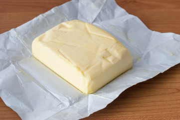 Butter cube on white paper with wooden background.