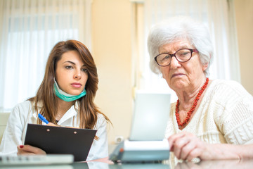 Nurse with clipboard writing results of blood pressure measurement of female senior patient.