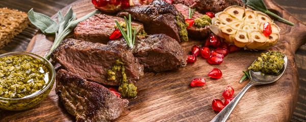 Kangaroo meat steak with green pesto and pomegranate on wooden cutting board. Healthy holiday food...