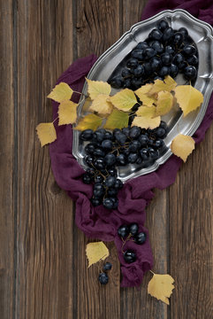 Grapes And Yellow Autumn Leaves On A Silver Platter. Rustic Wooden Background, Top View