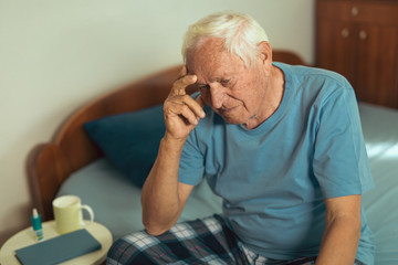 Senior Man Sitting On Bed At Home Suffering From Depression