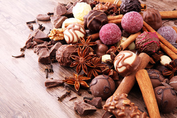 A selection of assorted chocolate truffle pralines on a wooden table with dark chocolate, cinnamon and anise.
