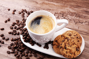 Coffee cup with chocolate cookies and coffee beans on wooden background