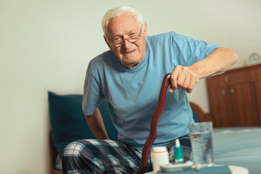 Senior man holding a walking stick and trying to get out of bed