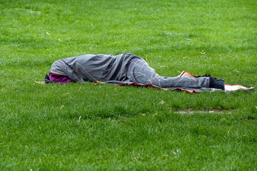 sleeping homeless man wrapped in gray blanket on green grass