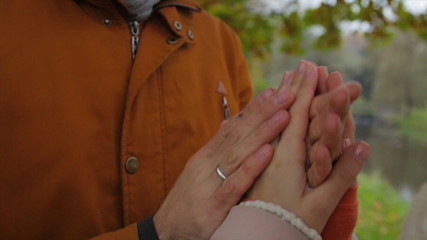 A man warms woman's hands. Bride and groom holding hands and warm each other in a park. Man and woman holding hands. warming hands.