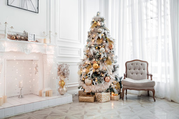 Classic white christmas interior with new year tree decorated. Fireplace with grey chair, clocks on...