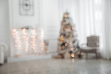 Unfocused classic white christmas interior with new year tree decorated. Fireplace with grey chair, clocks on the wall and presents under the tree