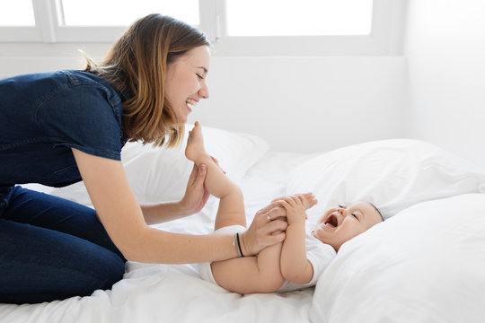 Young Mother Playing And Laughing With Baby On Bed