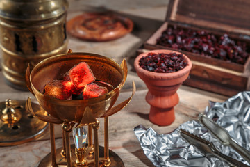 burning coals for Shisha Smoking are in the Golden bowl, made in the shape of a Lotus on the background of Smoking accessories