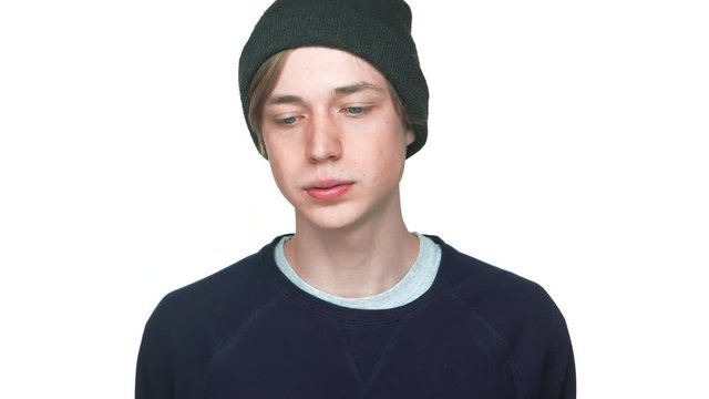 portrait of blue-eyed male teenager in sweatshirt and hat rolling eyes tired of something saying no negatively shaking head over white background closeup. Concept of emotions