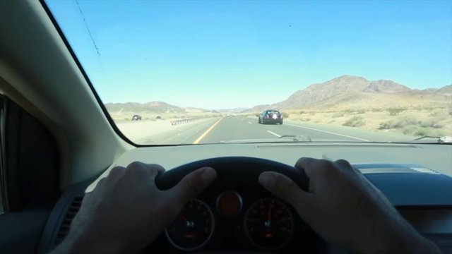 POV Of Man Driving By Mountains With Hands On Steering Wheel