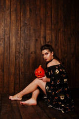 Black girl in dress with bright make-up and pumpkin against wooden background. Halloween theme.