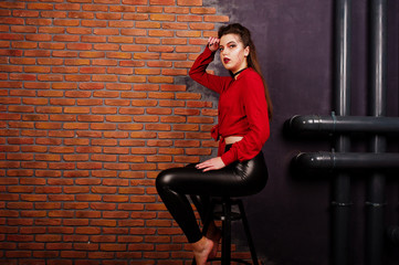 Fototapeta na wymiar Black girl in red shirt and leather pants with bright make-up posing at studio background brick wall. Halloween theme.