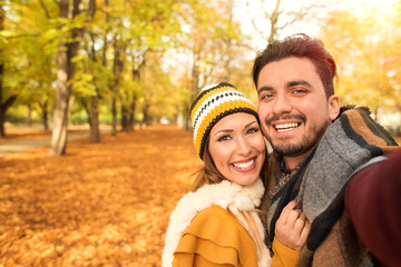 Beautiful couple taking a selfie at a park in autumn