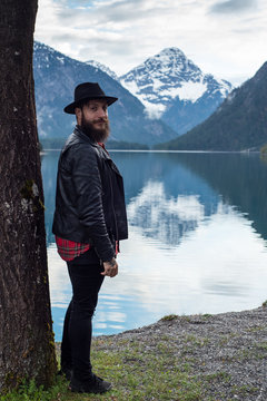 Stylish tattoed Hipster Man enjoys scenic mountain lake in Austria