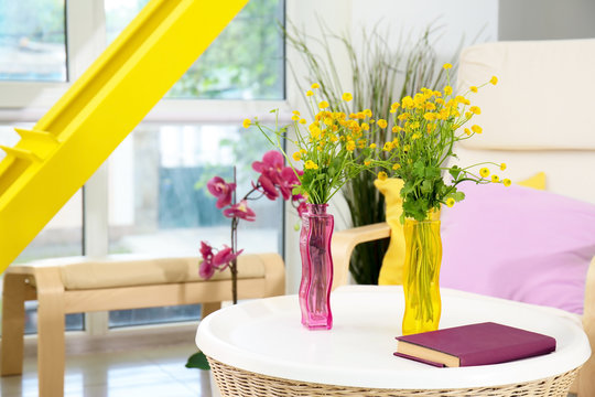 Vases with bouquets of beautiful flowers on table in room