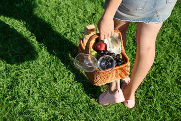 Woman holding wicker basket with picnic stuff outdoors