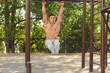 Handsome young man doing chin ups outdoors
