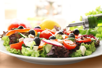Pouring olive oil onto plate with healthy salad in kitchen