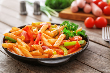 Pasta with sausage in portioned frying pan on wooden background