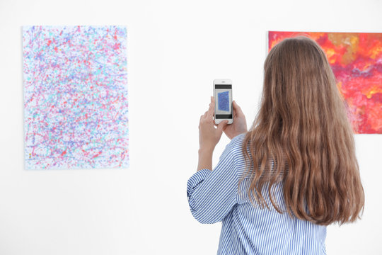 Young woman taking picture of painting in art gallery