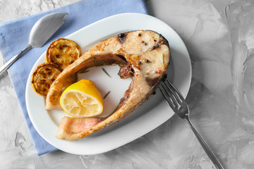 Ceramic plate with fried fish steak on grey background
